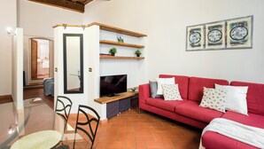 A living room with a red sofa, a TV on a wooden stand, a glass table, and a red-tiled floor.