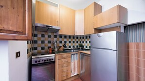 A compact kitchen with wooden cabinets, a stainless steel stove, a dishwasher, and a refrigerator.