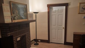 Een woonkamer met een open haard, een deur en een ingelijst schilderij aan de muur.