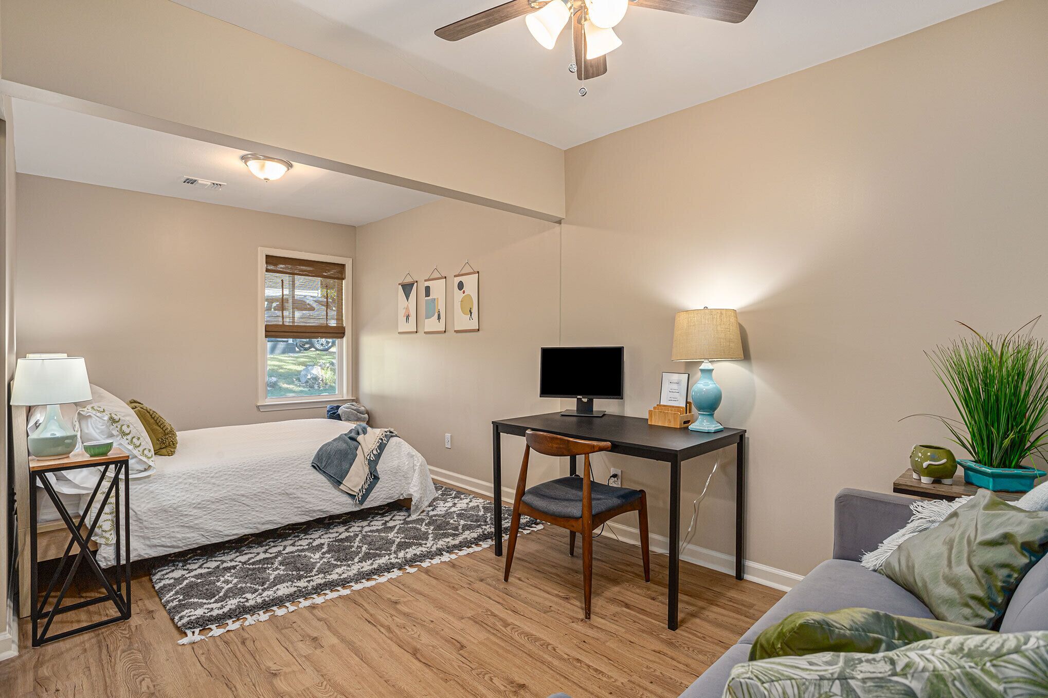 A bedroom with a bed, a desk, a chair, a ceiling fan, and a window with blinds.
