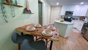 Cozinha moderna com armários brancos, mesa de jantar de madeira para quatro pessoas e uma ilha com micro-ondas e torradeira.