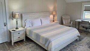 Une chambre à coucher comprenant un lit, deux tables de chevet, un bureau, une chaise et un ventilateur de plafond.