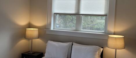 Een slaapkamer met een bed, twee nachtkastjes met lampen, een plafondventilator en een raam met jaloezieën.