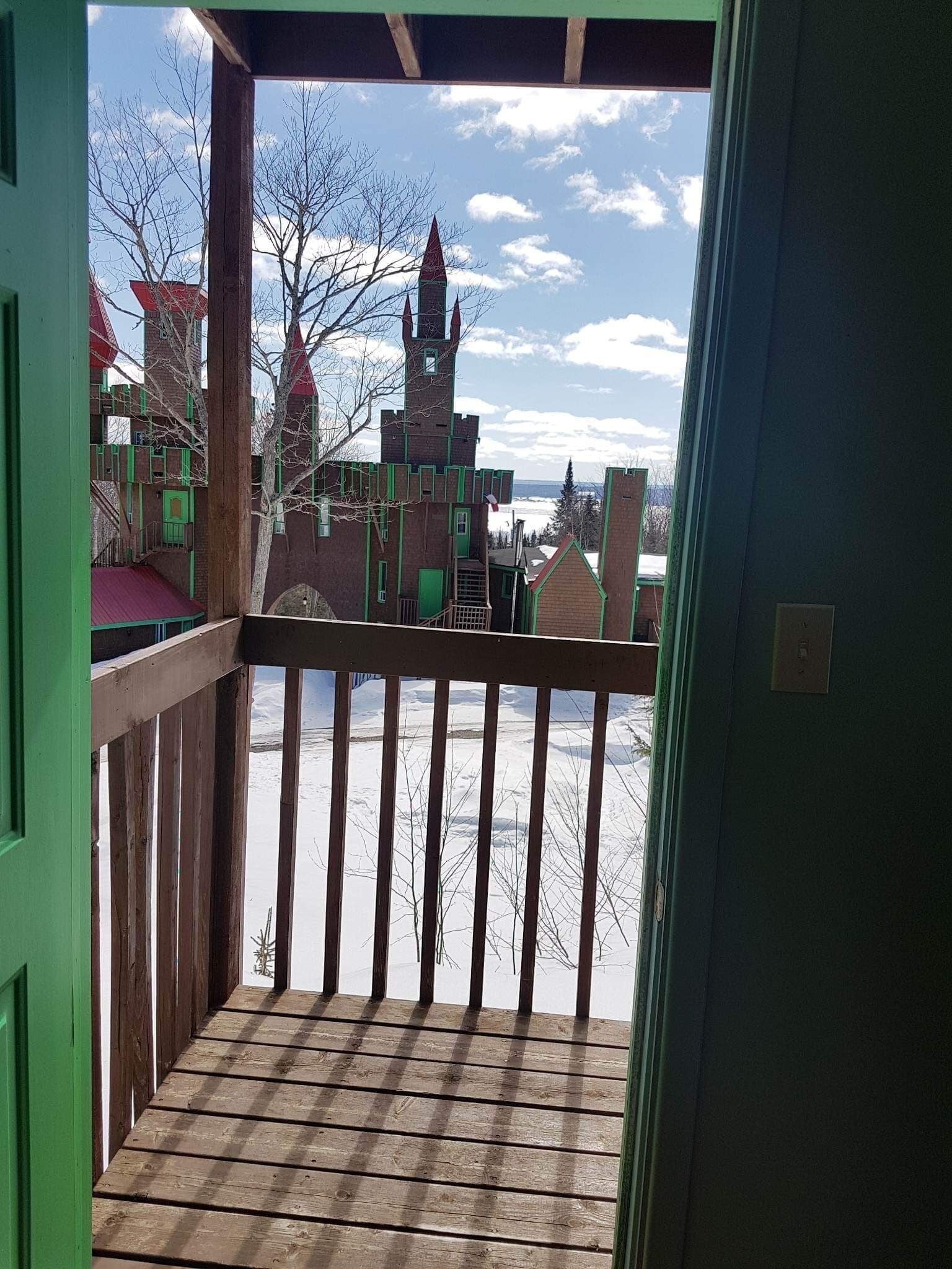 Un balcón de madera con vistas a un edificio que recuerda a un castillo y un paisaje nevado.