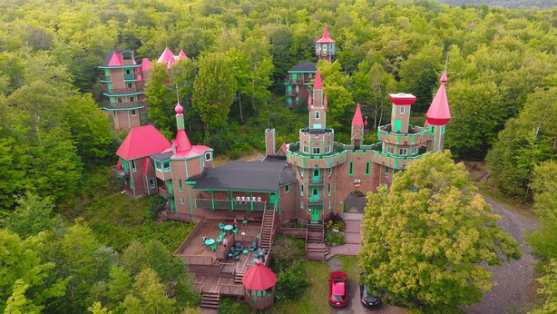 A castle-like structure with multiple towers and balconies, surrounded by dense forest. - Auberge Château Bahia (Escuminac)