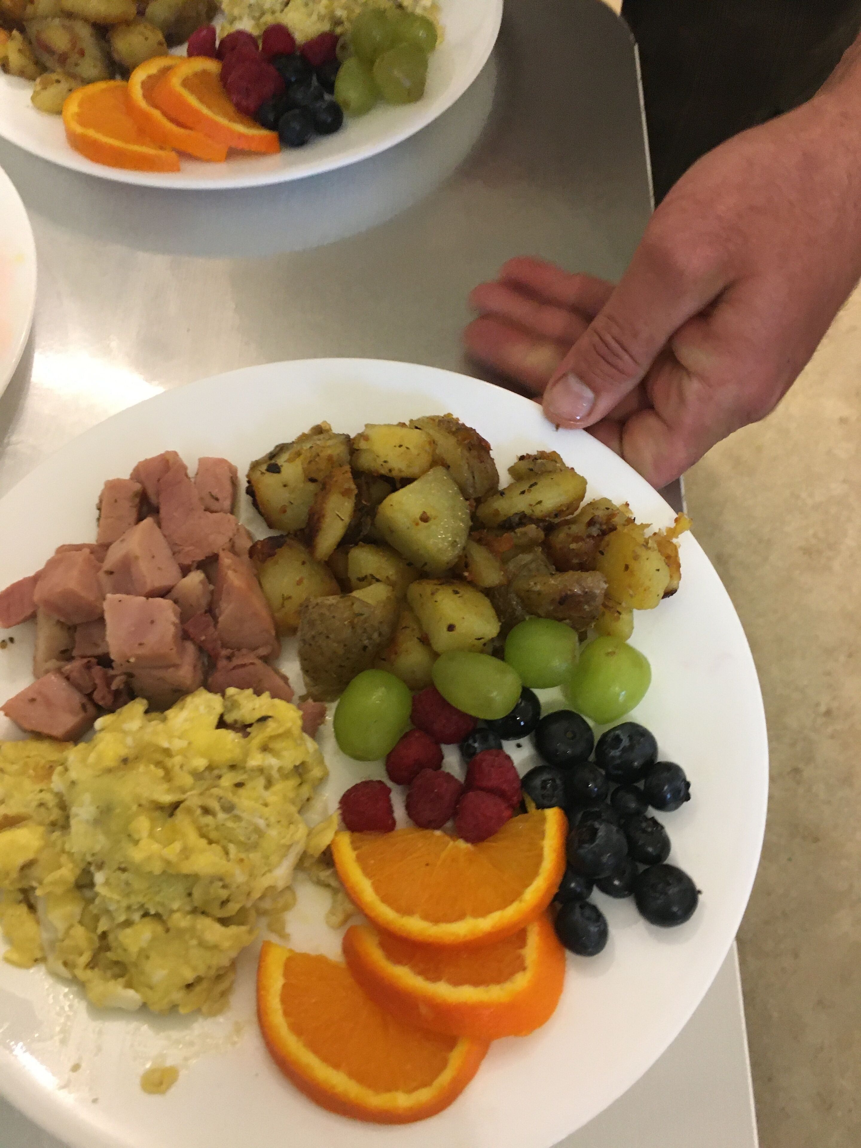 Un plato de comida con jamón, patatas, huevos y diversas frutas.