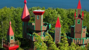 A castle-like structure with multiple towers and turrets, surrounded by lush greenery and overlooking a large body of water. - Auberge Château Bahia (Escuminac)