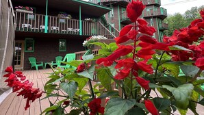 A wooden deck with green chairs, a building with a turret and red roof, and red flowers in the foreground. - Auberge Château Bahia (Escuminac)