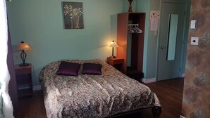 A bedroom with a bed, two bedside lamps, a wall-mounted artwork, a wardrobe, and a door with a mirror. - Auberge Château Bahia (Escuminac)