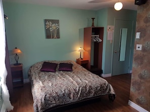 A bedroom with a bed, two bedside lamps, a wall-mounted artwork, a wardrobe, and a door with a mirror. - Auberge Château Bahia (Escuminac)