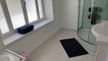 Un baño con inodoro, lavamanos, cabina de ducha de vidrio y una ventana con persiana decorativa.