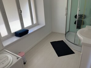 Un baño con inodoro, lavamanos, cabina de ducha de vidrio y una ventana con persiana decorativa.