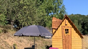 Een houten hut met een rieten dak, een tafel met stoelen, een grote parasol en een roze ligstoel.