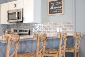 Una cocina con armarios blancos, un microondas y una mesa de comedor de madera con sillas.