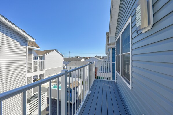 A narrow wooden deck with a metal railing, overlooking a residential area with houses and a clear blue sky.