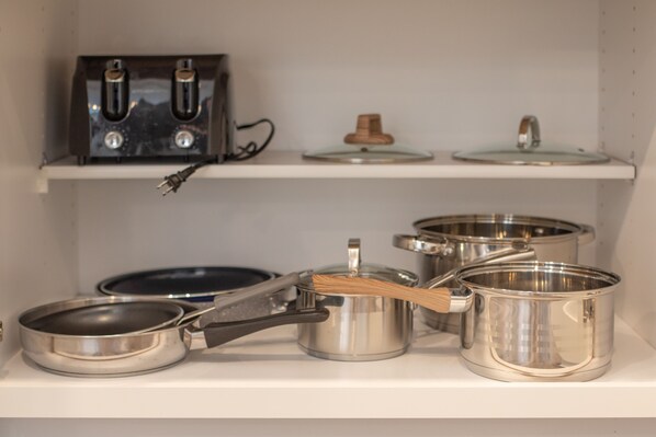 A kitchen shelf with stainless steel cookware, including pots, pans, and a whisk.