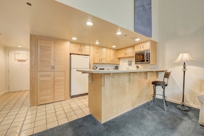Una cocina moderna con armarios de madera, un microondas integrado y una zona de bar con un taburete.