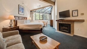 Un dormitorio con cama, mesitas de noche, televisor, chimenea y un ventanal grande.