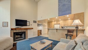 Una sala de estar con chimenea, televisor, comedor con barra y cocina.