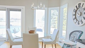 Et moderne spiseområde med et glasbord, hvide stole og et stort vægur.
