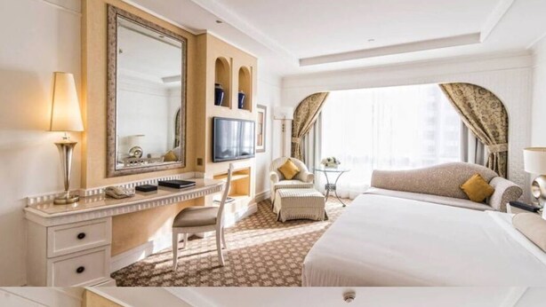 Quarto de hotel com uma cama grande, uma escrivaninha com cadeira, uma televisão e um espelho grande.