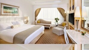 Quarto de hotel com uma cama grande, um sofá, uma mesinha e uma televisão.