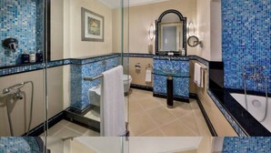 Casa de banho com cabine de chuveiro em vidro, lavatório com painel de azulejos azuis, banheira e sanita.