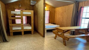 Una habitación de madera con literas, una cama individual, una mesa de madera y una ventana con cortinas.