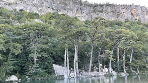 A natural landscape with a body of water, trees, and a rocky cliff. - Zubers - CA -F Cabin F (Concan)