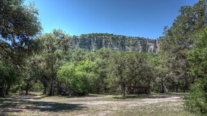 A natural landscape with a rocky cliff, dense trees, and a wooden structure. - Zubers - CA -H Cabin H (Concan)