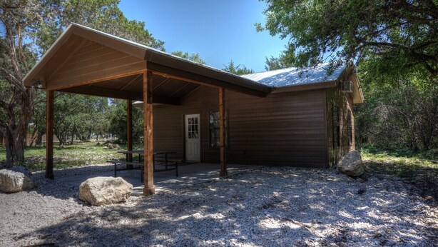 A rustic cabin with a covered porch, a door, and a window. - Zubers - CA -H Cabin H (Concan)