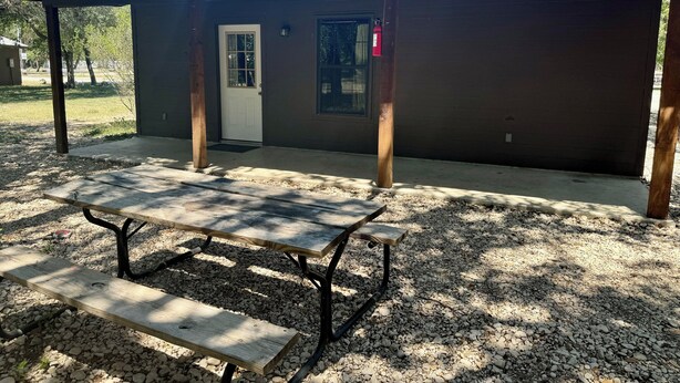 A small building with a covered patio area, a picnic table, and a fire extinguisher mounted on the wall.
