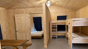 Eine Holzhütte mit Etagenbetten, einem Einzelbett, einem Tisch und einem Deckenventilator.