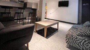 Un salon moderne avec un canapé, une table basse et un lit à motifs zébrés. Il y a également un coin cuisine équipé d’un micro-ondes et d’un téléviseur fixé au mur.