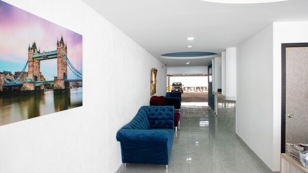 Un couloir orné d’un grand tableau représentant un pont, avec un canapé bleu et un comptoir d’accueil.