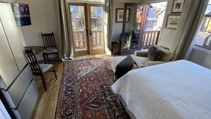 A bedroom with a large bed, a sofa, a wooden chair, a small table, a TV, and a view of the outside through a sliding glass door. - Studio in upscale, intimate Black Mountain neighborhood (Black Mountain)