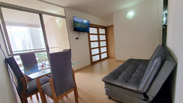 A living room with a sofa, a dining table with chairs, a TV mounted on the wall, and a sliding glass door leading to a balcony. - Cartagena functional apartment 2 blocks from the beach Marbella (Cartagena de Indias)