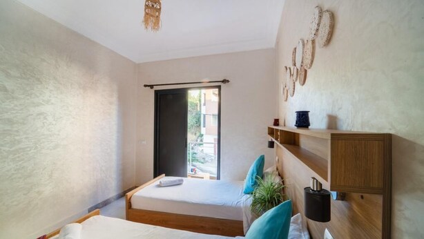 Quarto moderno com duas camas, uma cabeceira de madeira, uma planta pequena e uma janela com vista para o exterior.