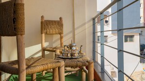 Varanda com cadeira de vime, uma mesa pequena com bandeja e vista para edifícios.