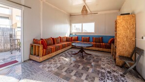 A spacious living area with a large L-shaped sectional sofa, a round coffee table, and a wooden accent wall. - Spacious 4-Bed Apartment with Rooftop & Courtyard – Taghazout bay (Souss-Massa 80000)