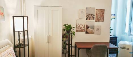 A bedroom with a bed, a desk, a chair, a wardrobe, and a small potted plant.