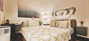 Une chambre d’hôtel comprenant un lit, un bureau, une chaise, une commode, un téléviseur fixé au mur et un grand tableau abstrait.