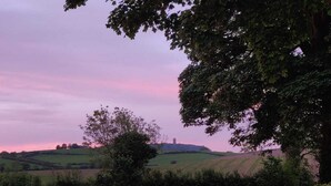 Ländliche Landschaft mit sanften Hügeln, einem entfernten Turm und einem Baum im Vordergrund.