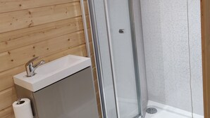 Ein Badezimmer mit Holzboden, einem weißen Waschbecken, einer Toilettenpapierrolle und einer Duschkabine mit Glastür.