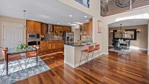 A spacious kitchen with wooden cabinets, a central island, and a dining area with a glass table and chairs. - Aurora Manor with Breathtaking Views (Aurora)