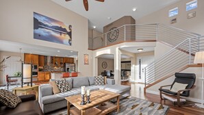 A spacious living area with a wooden coffee table, grey sofa, and a black leather chair. A staircase with a railing leads to an upper level. - Aurora Manor with Breathtaking Views (Aurora)