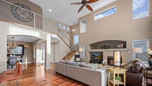 A spacious living area with a large gray sectional sofa, a brown leather chair, a wooden coffee table, and a fireplace. A staircase leads to an upper level with a balcony. - Aurora Manor with Breathtaking Views (Aurora)