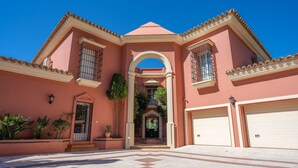 Um edifício rosa com um arco central, duas portas de garagem e um pátio com azulejos.