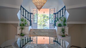 Uma escadaria imponente com guarda-corpo de vidro, que leva a um espaço aberto com plantas e vista para o verde lá fora.