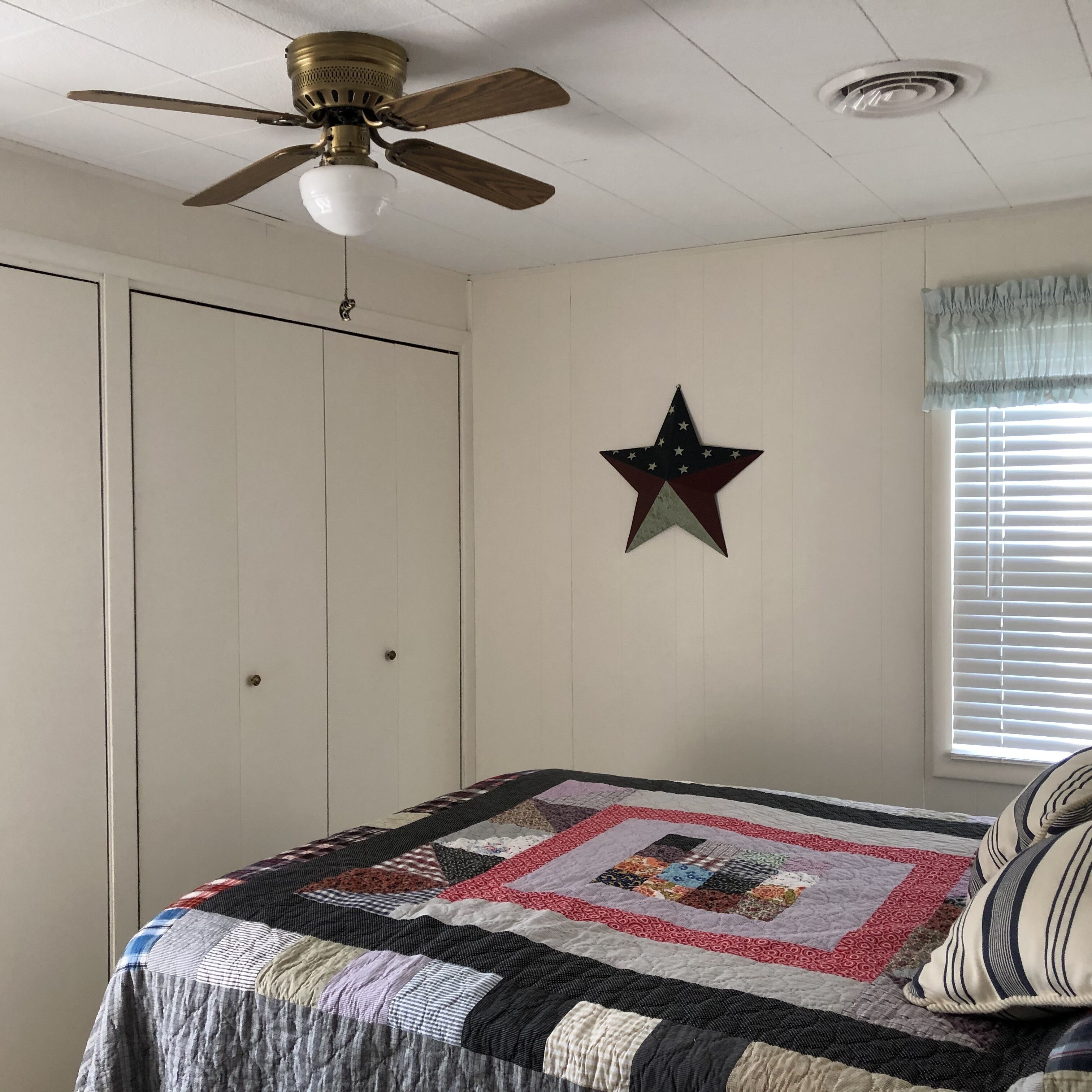 Een slaapkamer met een bed, een plafondventilator, een sterren decoratie en een raam met zonwering.